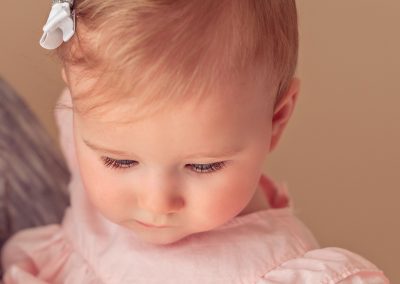 First and Forever Photography, Iveta Dietz, photography by Iveta Dietz, eyelashes, blue eyes, baby, baby girl, bow, pink dress, baby lips, close up, best newborn photographer, best baby photographer, best St. Charles photographer, St. Louis photographer, posed baby, baby's first year, safe posing, safety first, comfortable posing, cute baby, happy baby, brown background, cute look, big eyes,