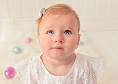 First and Forever Photography, Iveta Dietz, photography by Iveta Dietz, eyelashes, blue eyes, baby, baby girl, bow, pink dress, baby lips, close up, best newborn photographer, best baby photographer, best St. Charles photographer, St. Louis photographer, posed baby, baby's first year, safe posing, safety first, comfortable posing, cute baby, happy baby, white background, cute look, big eyes, sitting baby