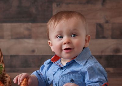 First and Forever Photography, Iveta Dietz, photography by Iveta Dietz, easter, carrots, basket, blue eyes, baby, baby boy, brown wooden background, best newborn photographer, best baby photographer, best St. Charles photographer, St. Louis photographer, posed baby, baby's first year, safe posing, safety first, comfortable posing, cute baby, happy baby, cute look, big eyes, blue shirt